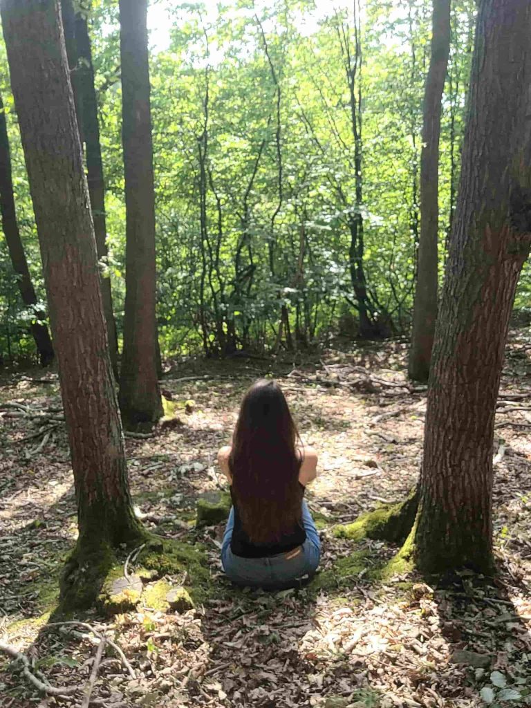 Frau sitzt im Wald zwischen zwei Bäumen